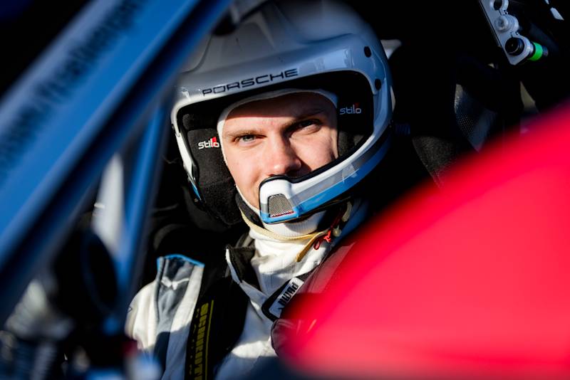 Driver in cockpit wearing Porsche racing helmet and suit, ready for the drive in sunny weather.