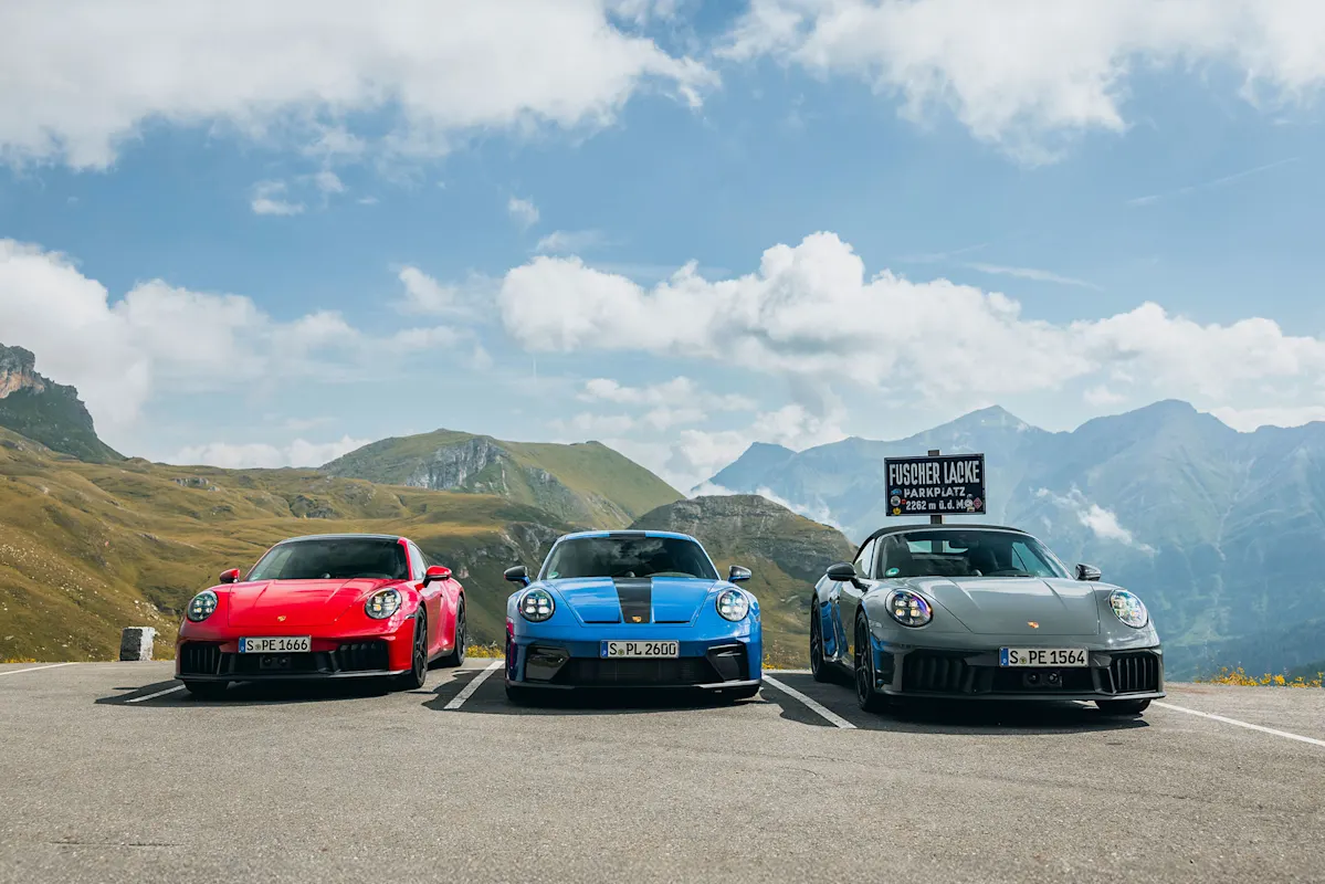 Drei Porsche nebeneinander auf Bergstraße mit Aussicht.