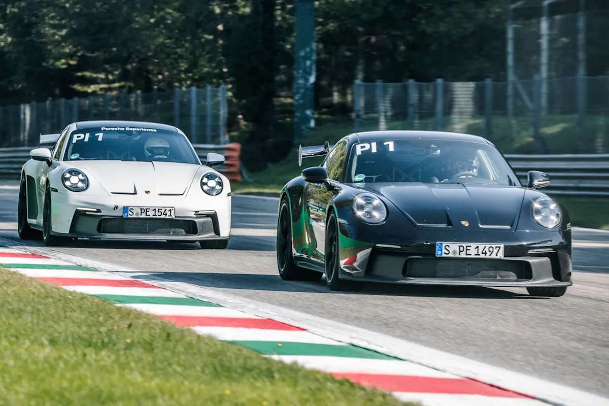 A black Porsche 911 GT3 and a white Porsche 911 GT3 drive in line on a race track on a sunny day.