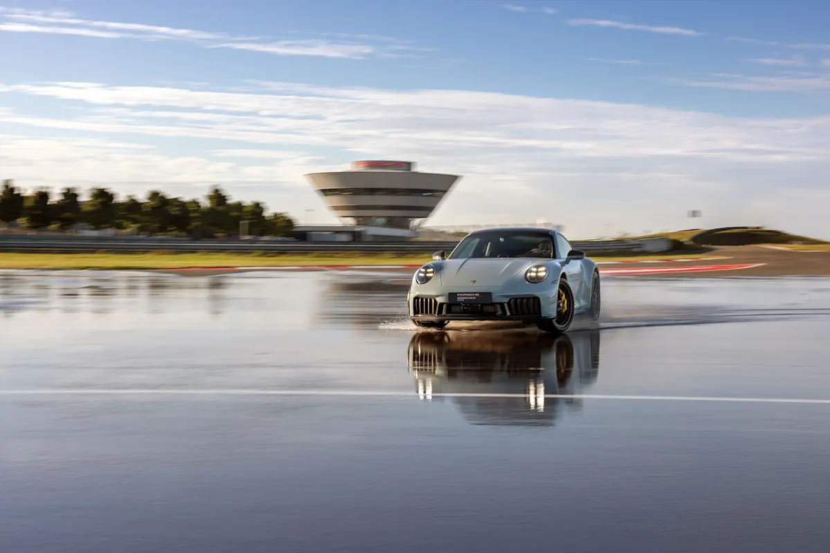 Dynamic driving training with a Porsche on a wet test track in front of a modern building.