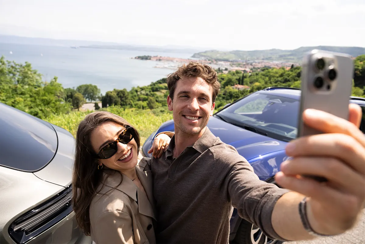 Paar macht Selfie bei zwei Autos an malerischer Küste.