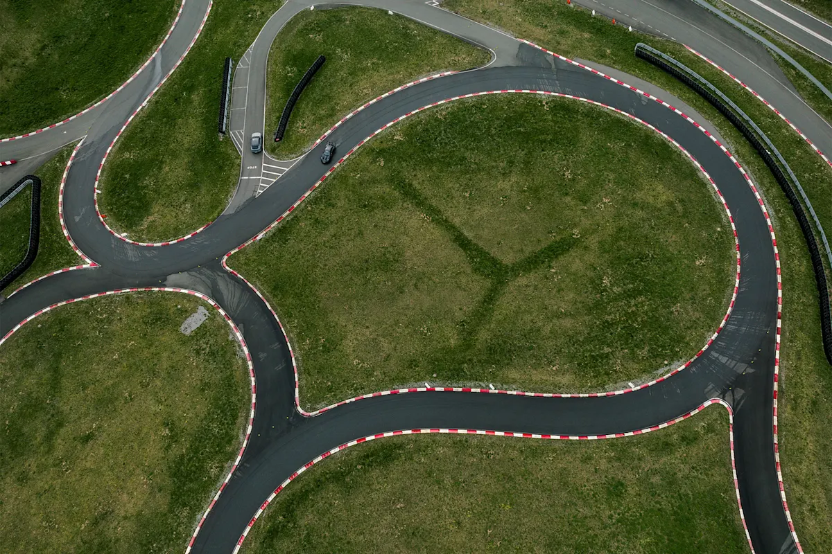 Aerial view of Porsche racetrack with red and white curbs, grass, and parked cars.