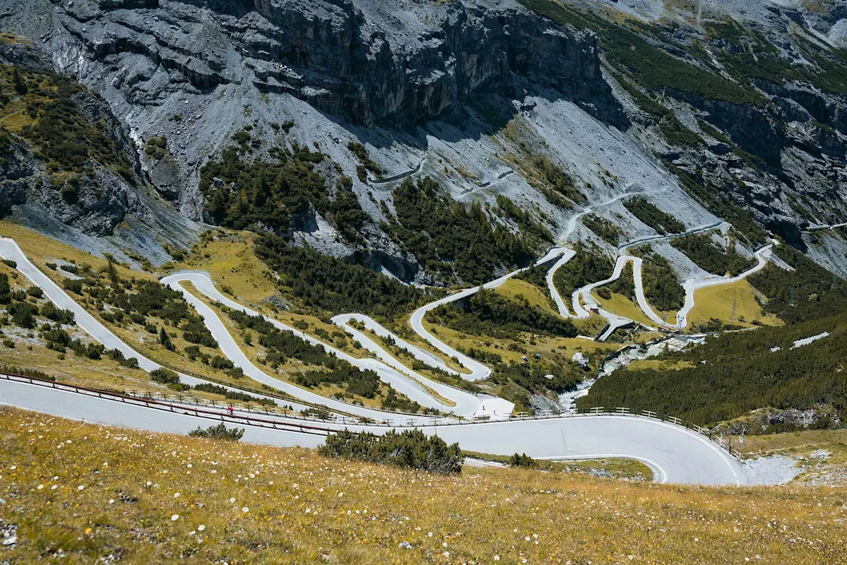 Gebirgsstraße mit scharfen Kurven, Felsen und Grün.