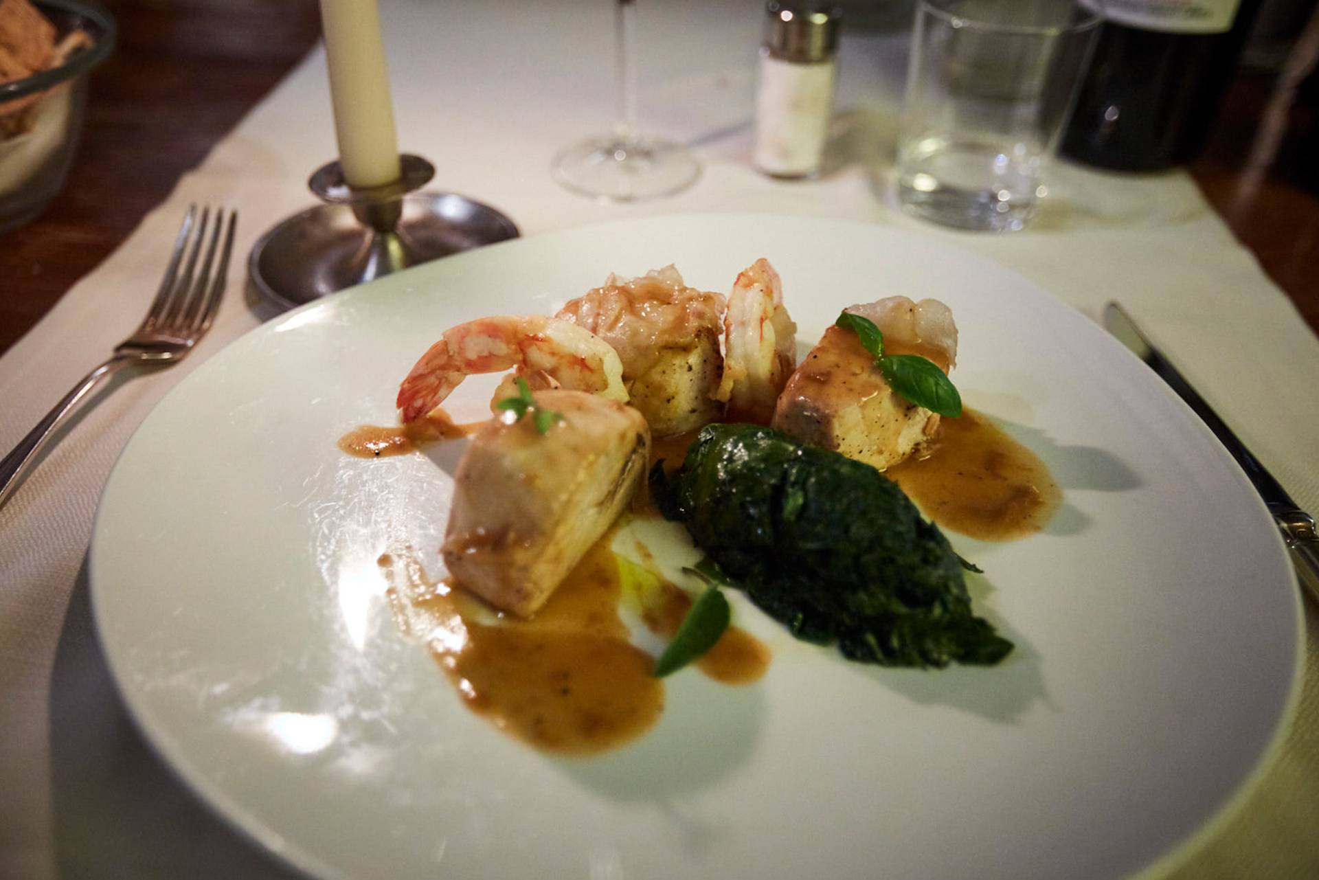 Teller mit Garnelen, Fisch, Soße, Spinat und Kerze auf dem Esstisch.