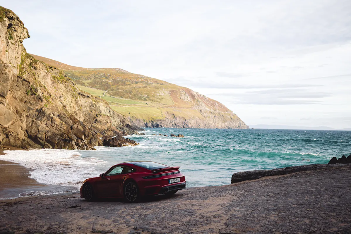 Roter Porsche am Meer mit Wellen und Hügeln dahinter.