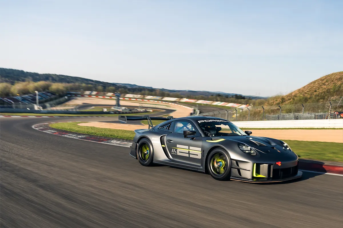 Sleek Porsche sports car speeds on track with scenic backdrop and clear blue sky.