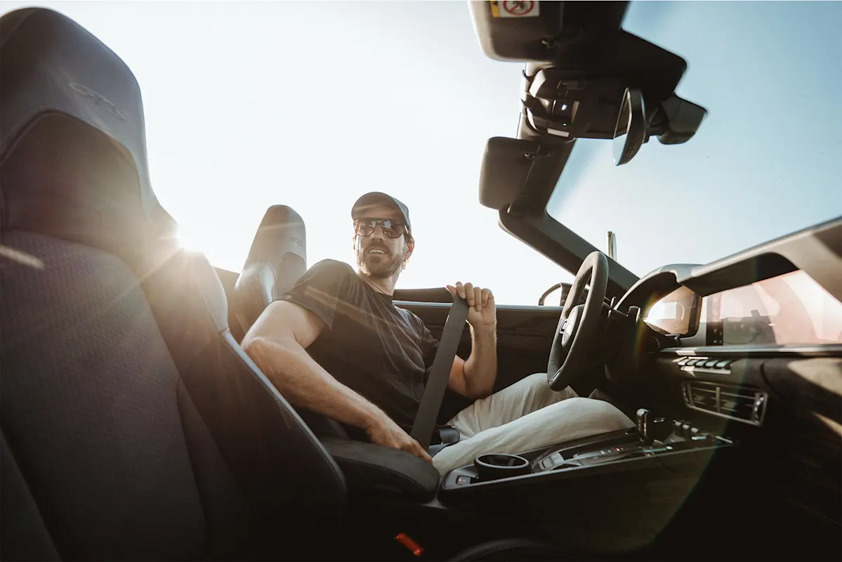 Mann schnallt sich in einem Porsche Cabrio unter Sonnenlicht an