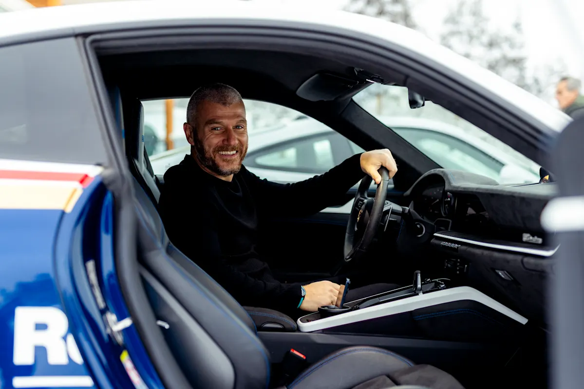 A man in a car's driver seat, smiling and looking at the camera.