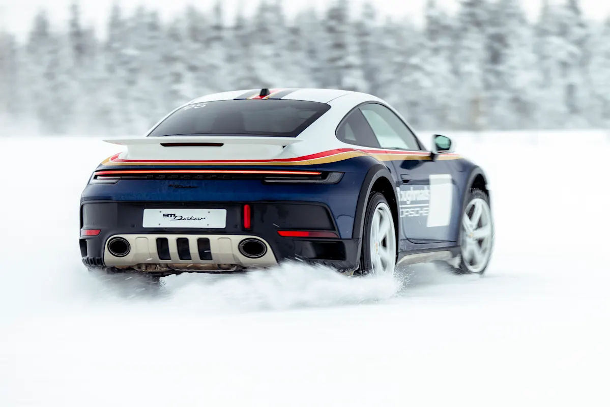 Porsche sports car speeding on snowy road with blurred trees, kicking up snow.