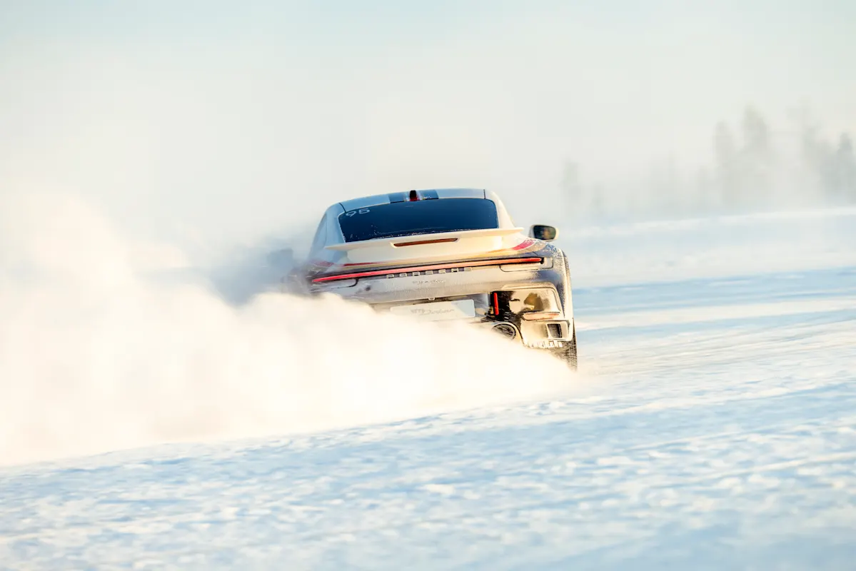 White Porsche drifts on snowy track, creating large snow cloud.