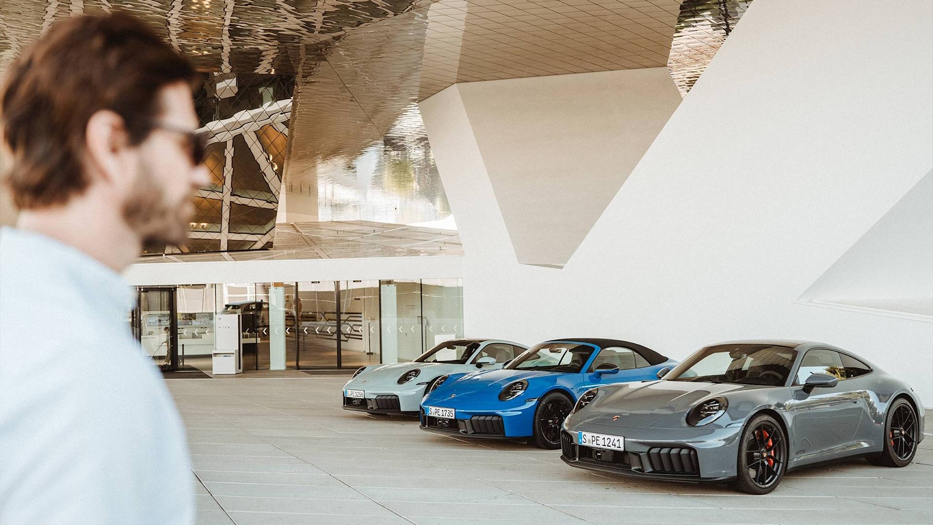 Mann mit Sonnenbrille betrachtet drei Porsche vor einem Gebäude.
