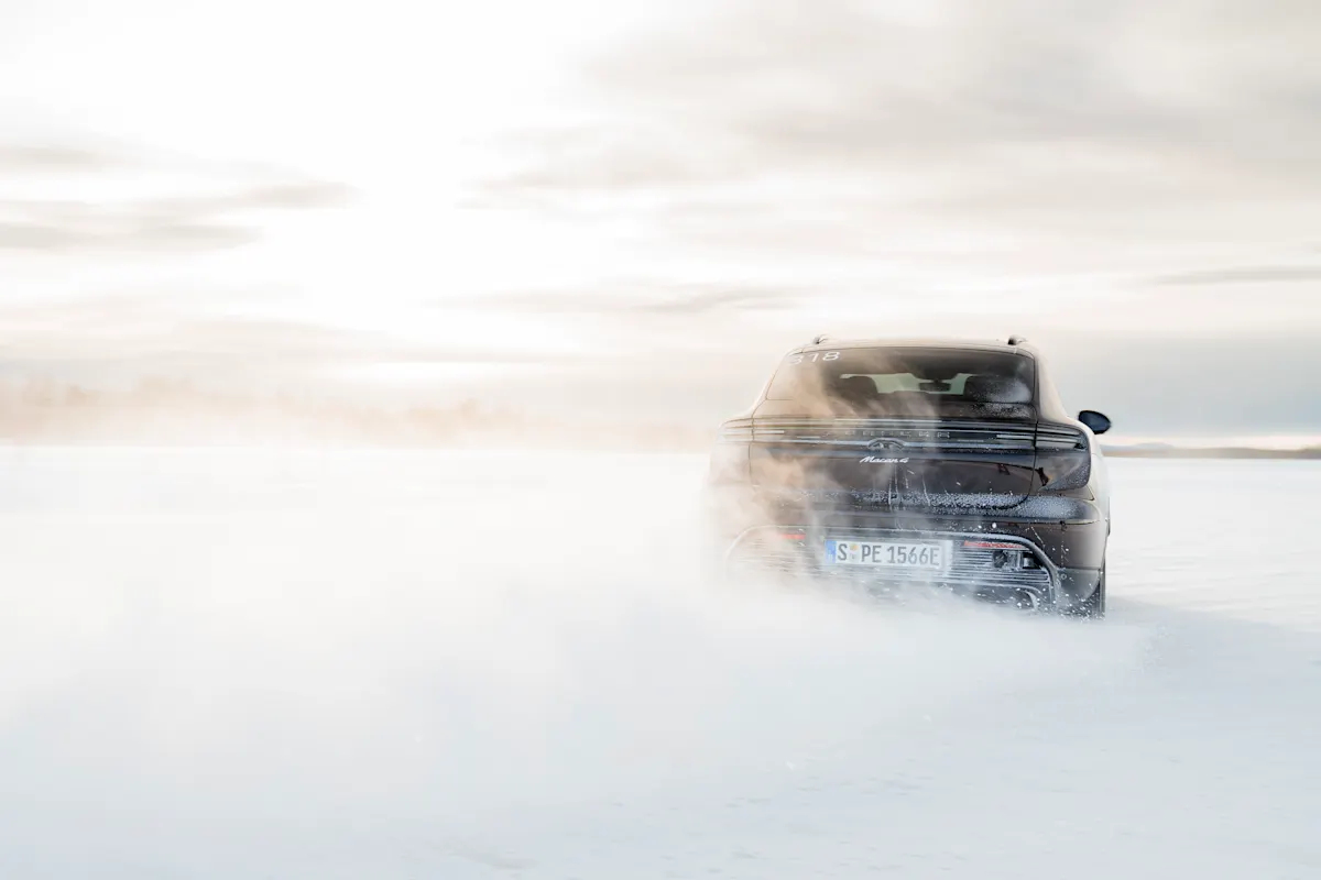 Rear view of a Porsche Macan Electric kicking up snow on a winter track at sunset.