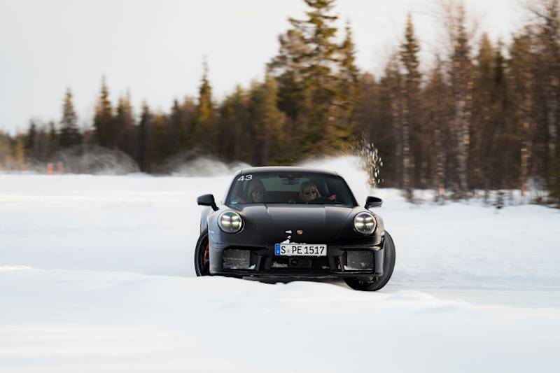Schwarzer Porsche driftet im Schnee mit Bäumen dahinter.