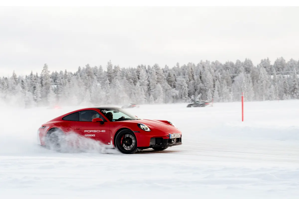A red Porsche drifting on snowy track, near snow-covered trees and landscape.