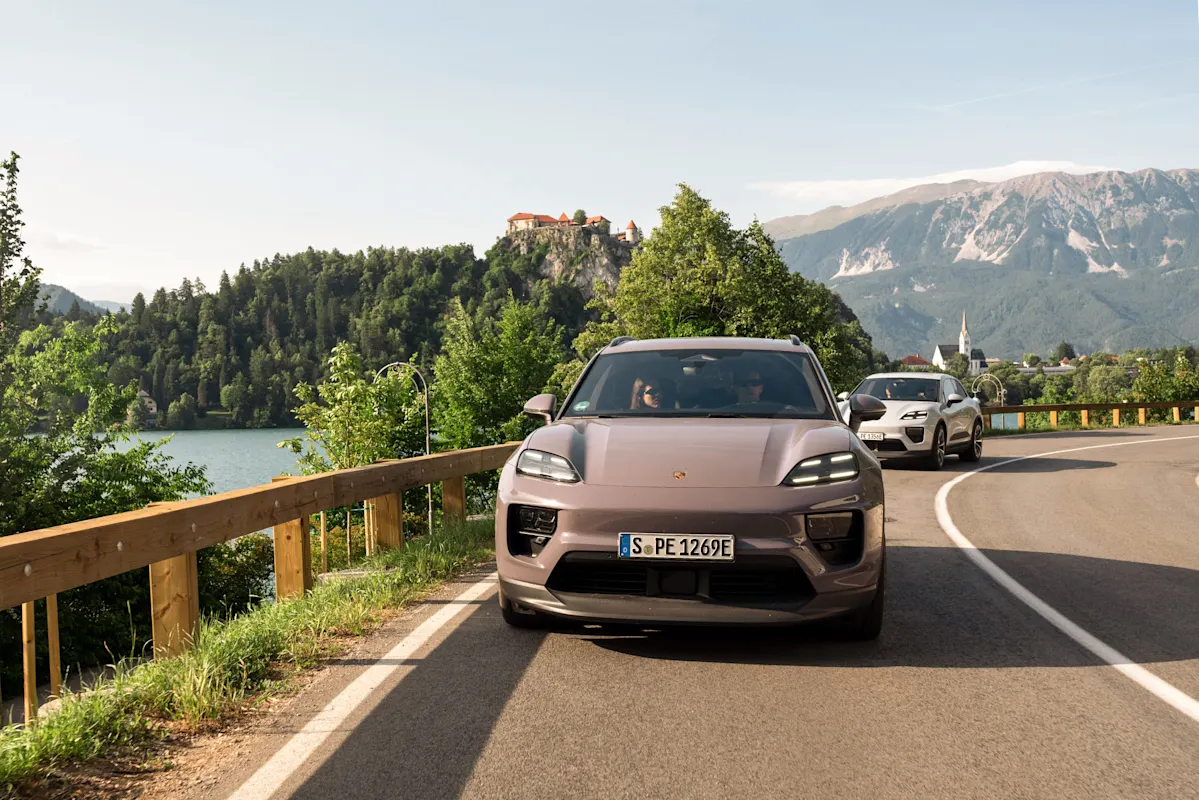 Silberner Porsche SUV an Seestraße mit Bergen & Schloss.