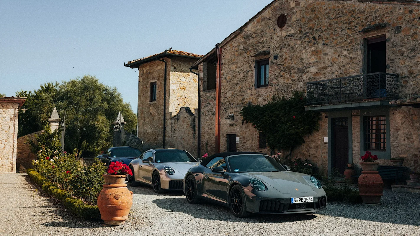 Drei graue Porsche vor einem Steingebäude mit Terrakottatöpfen.