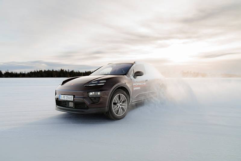 Porsche SUV rast im Schnee, Wald und Wolken dahinter.
