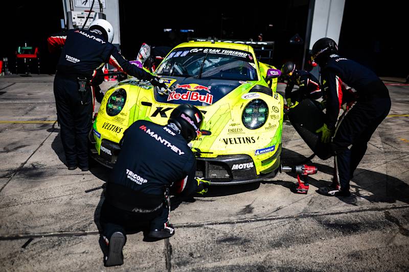 Porsche pit crew servicing bright yellow and green 911 race car at a pit stop with equipment.