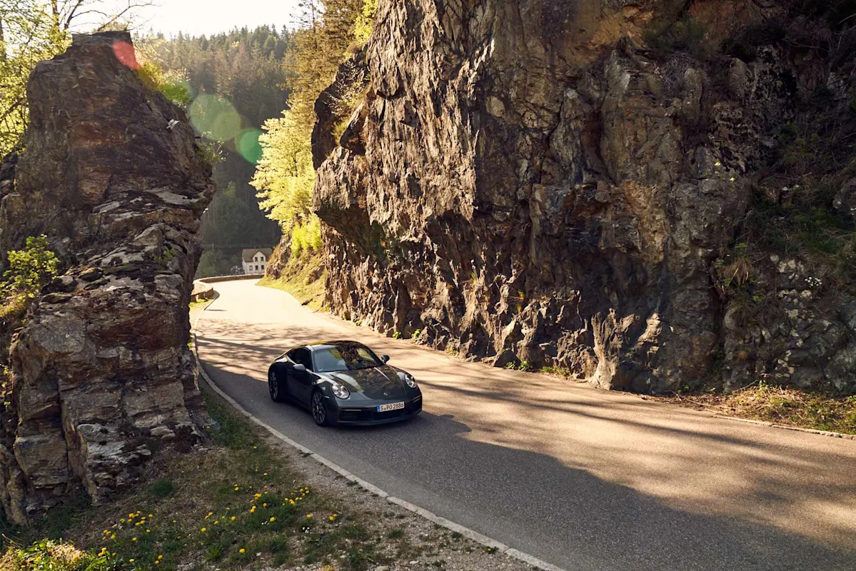 A Porsche on a winding mountain road between high cliffs in the sunshine.