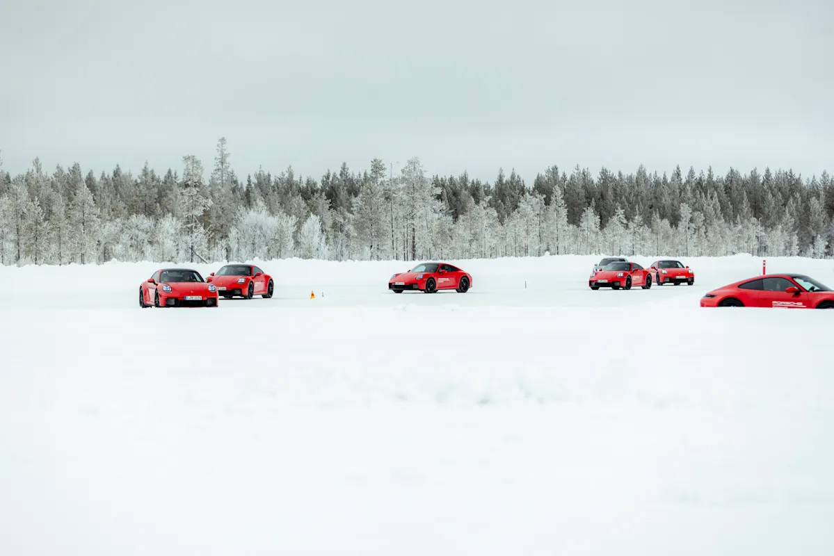 Red Porsche sports car race on snowy track near snow-covered forest.