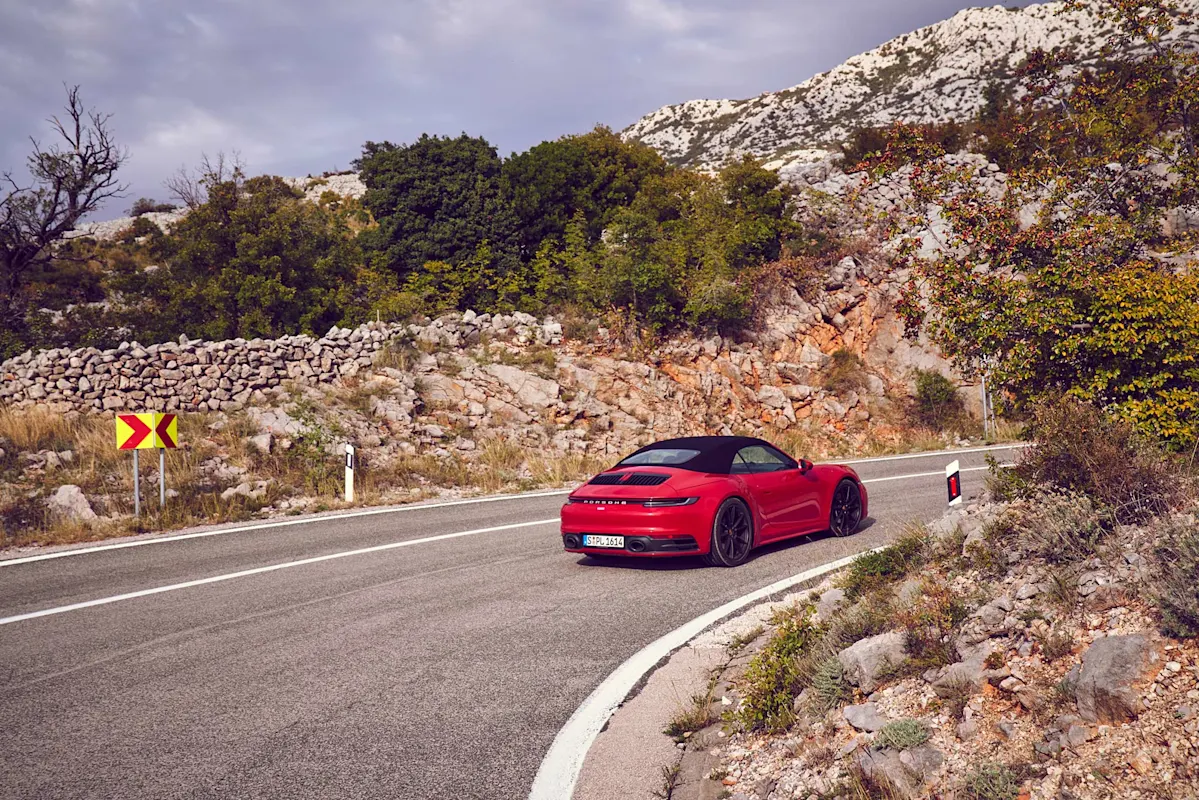 Roter Porsche Cabrio auf Bergstraße mit malerischem Panorama.