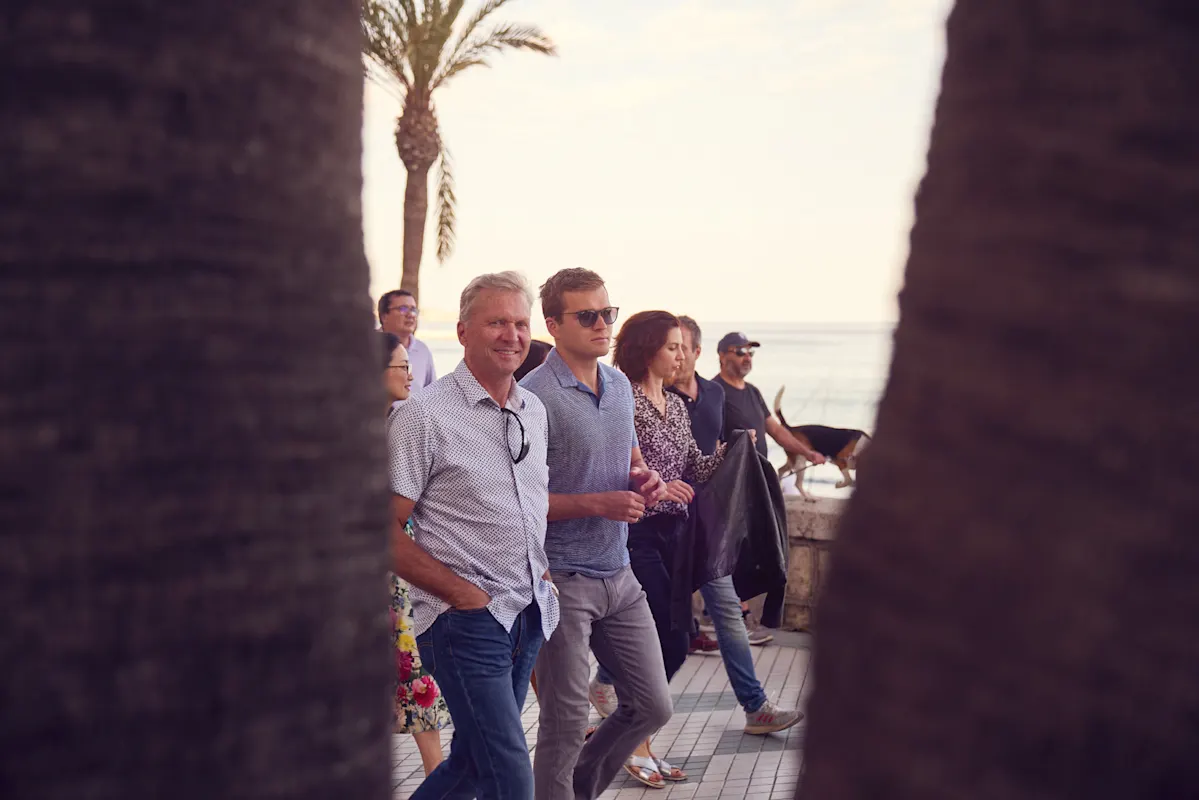 Menschen laufen auf sonniger Strandpromenade mit Palmen.
