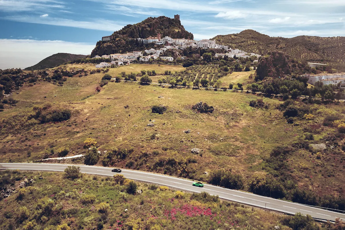 Eine kurvige Straße an einem grünen Hügel, Dorf, Felsen unter blauem Himmel.