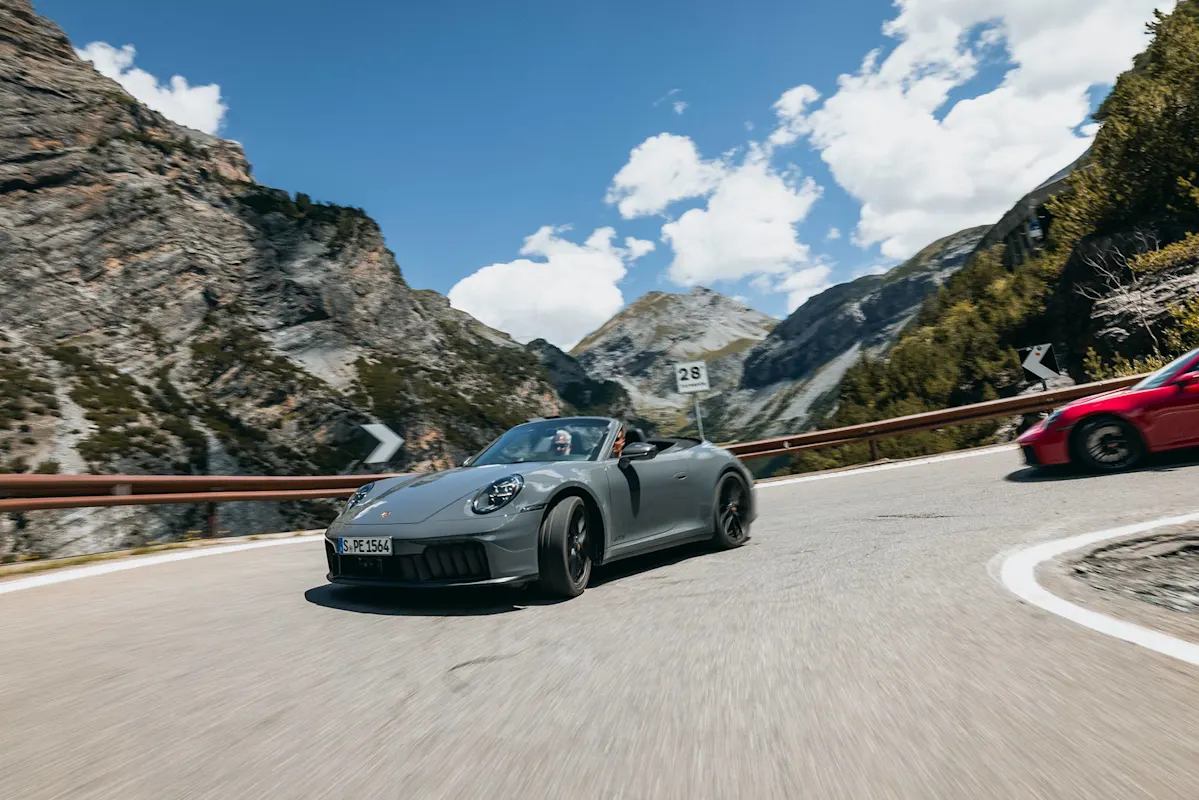 Grauer und roter Porsche auf Bergstraße unter blauem Himmel.