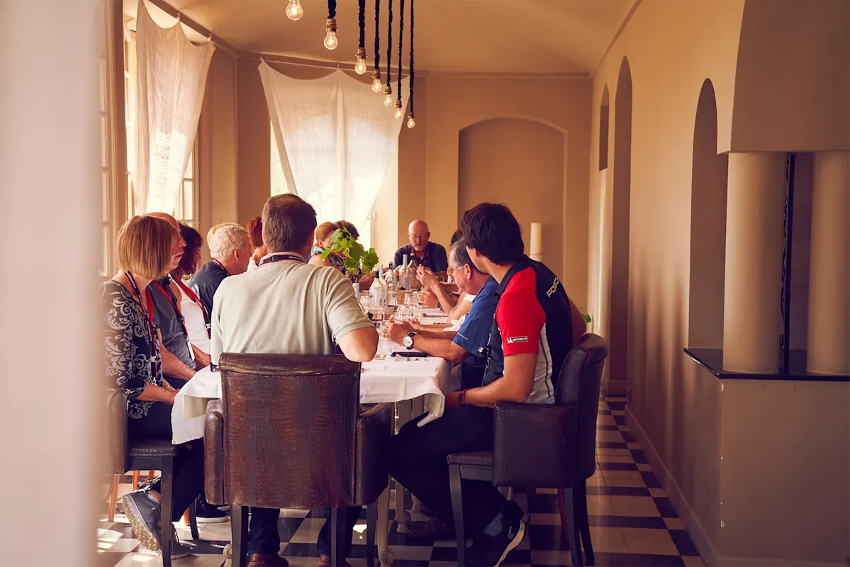 Personen essen und plaudern an einem Tisch in einem sonnigen Raum.