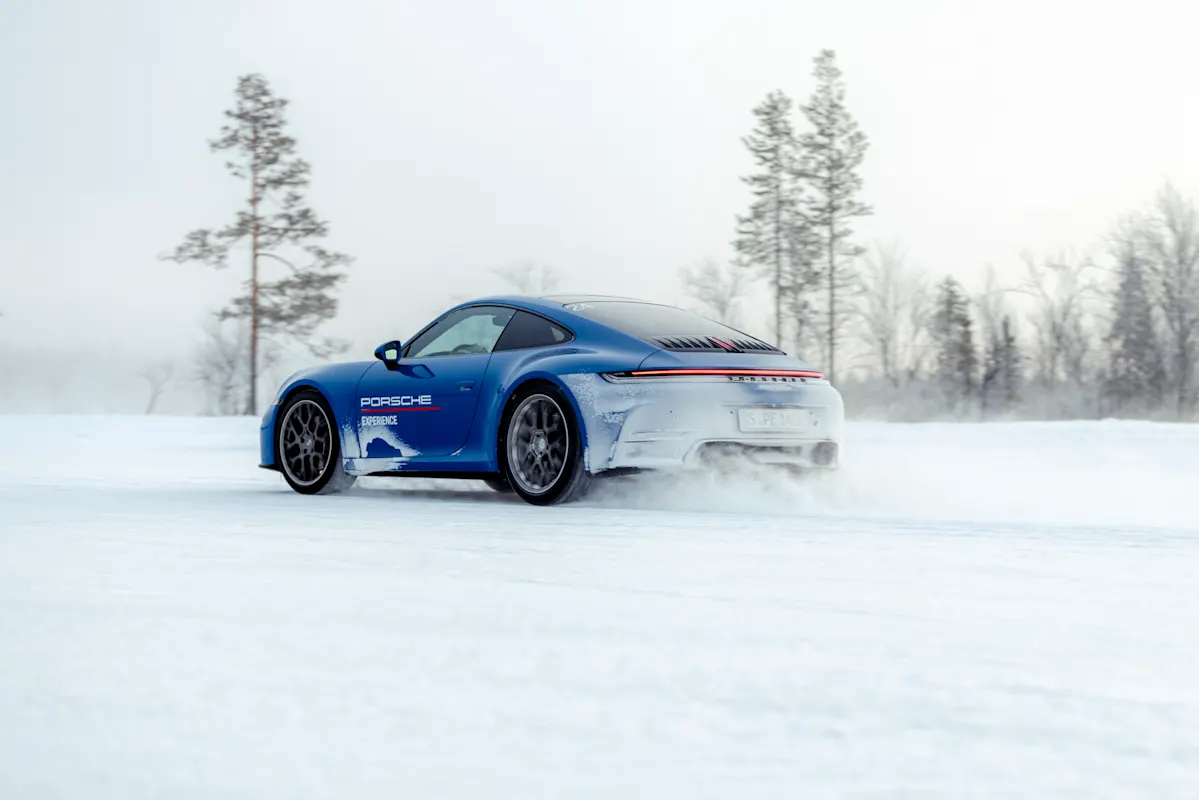 Blue Porsche 911 drifting dynamically on icy track, snowy landscape and forest in the background.