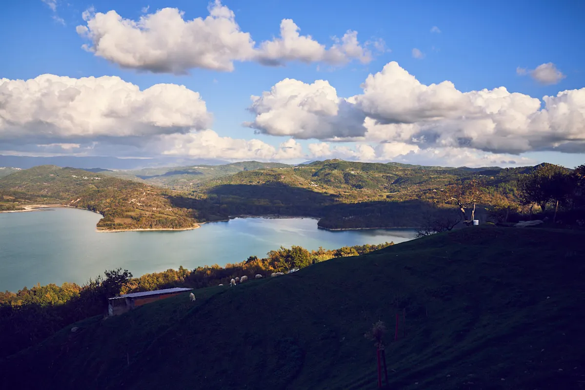See umgeben von Grün unter teils bewölktem blauen Himmel.