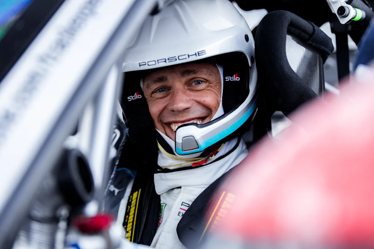 Smiling driver in white helmet sits in Porsche, ready for race.
