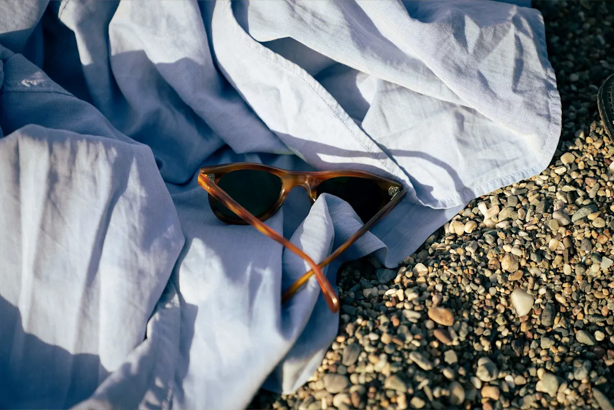 Brown sunglasses on a blue shirt at a pebbled beach.