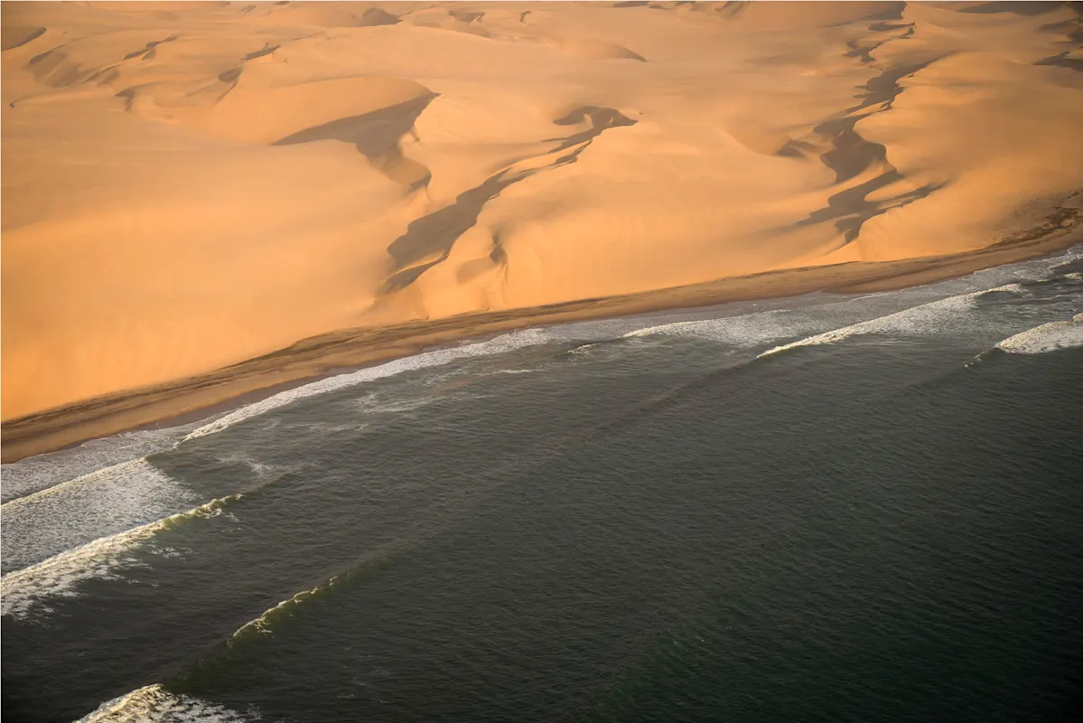 Luftblick, wo Meereswellen in Sonnenlicht auf Dünen treffen.