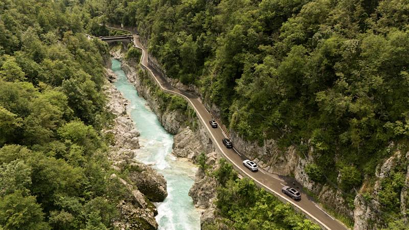 Autos auf Bergstraße bei türkisem Fluss im Wald.