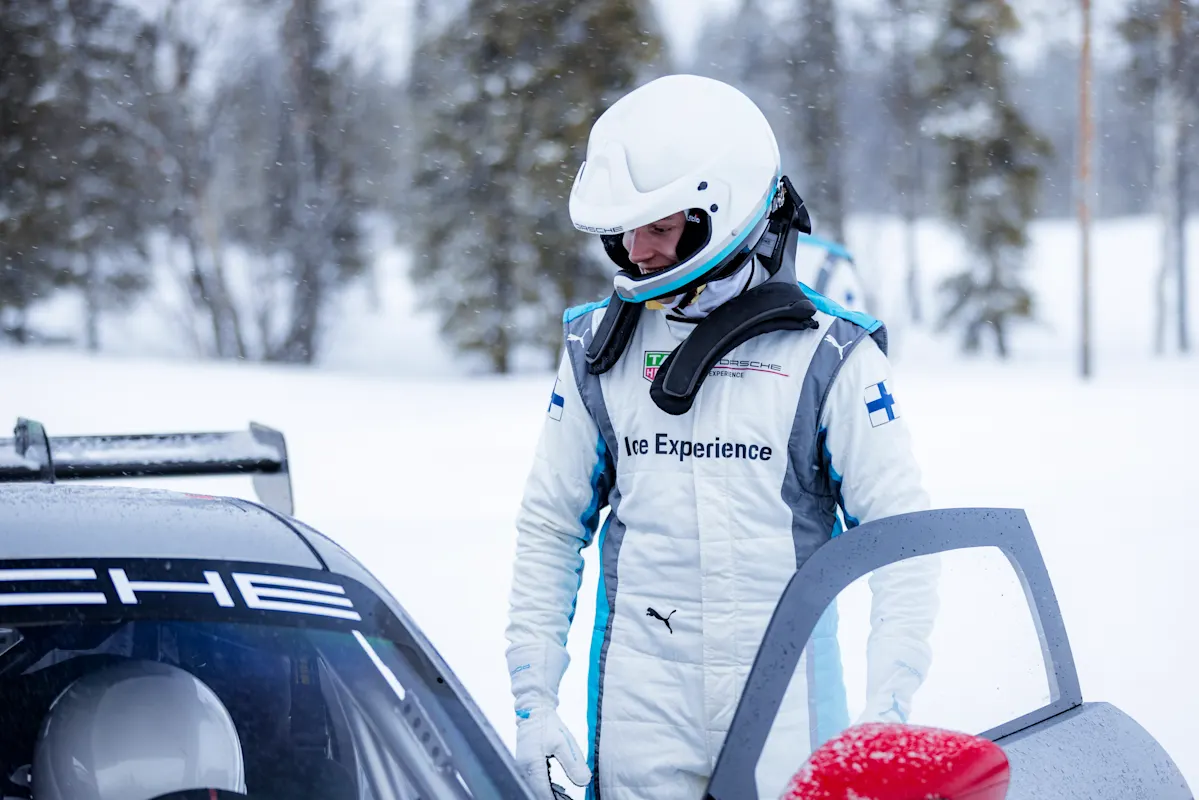 A driver next to a Porsche in snowy forest.