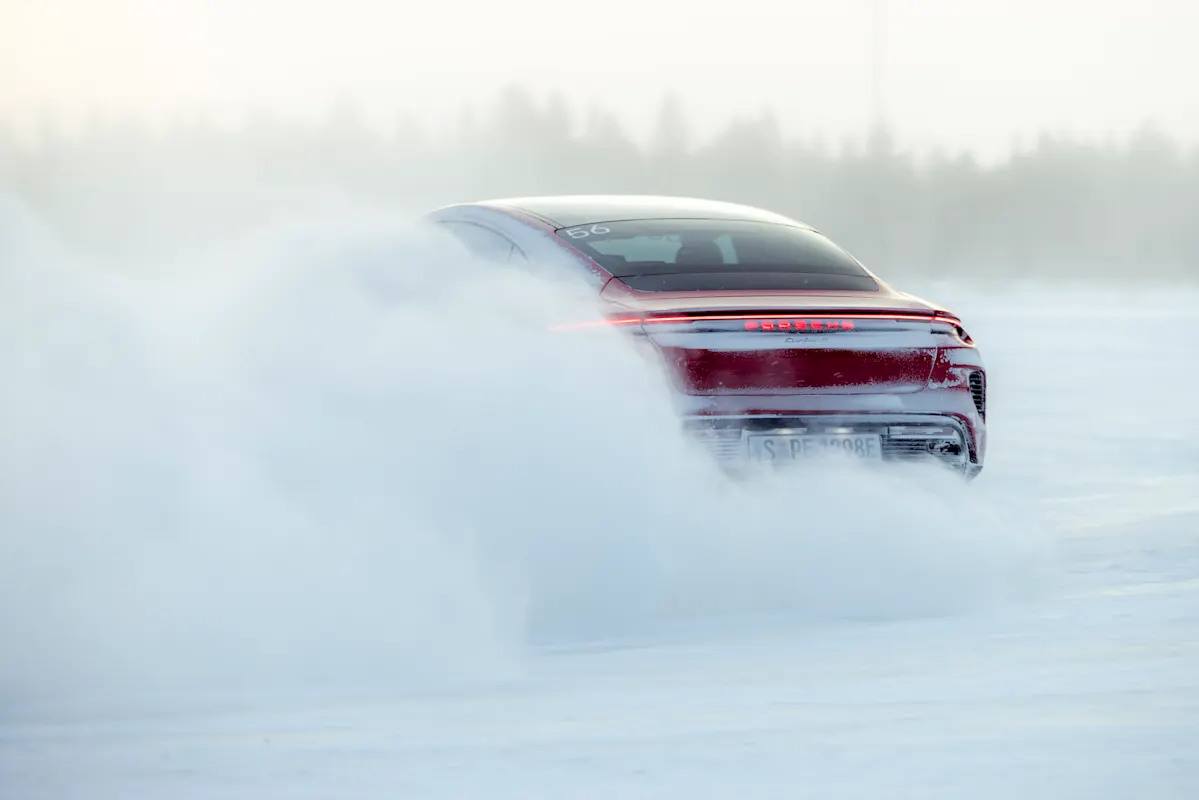 A red Porsche skids on a snowy road, kicking up snow, with blurred trees.