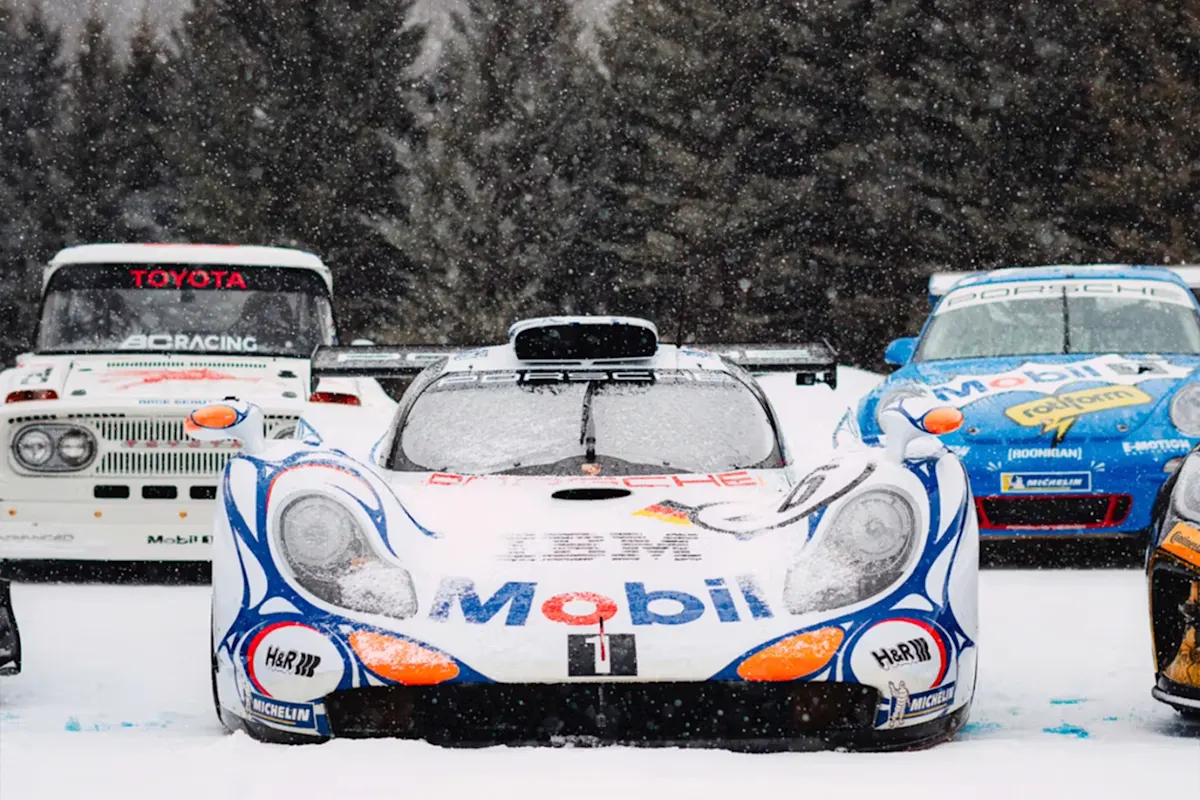 Racing Porsche in snowy conditions next to snow-covered trees.
