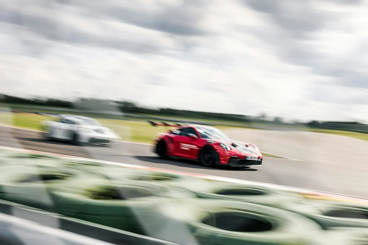 Race car speeding on a track with blurred background and green tire barriers in foreground.