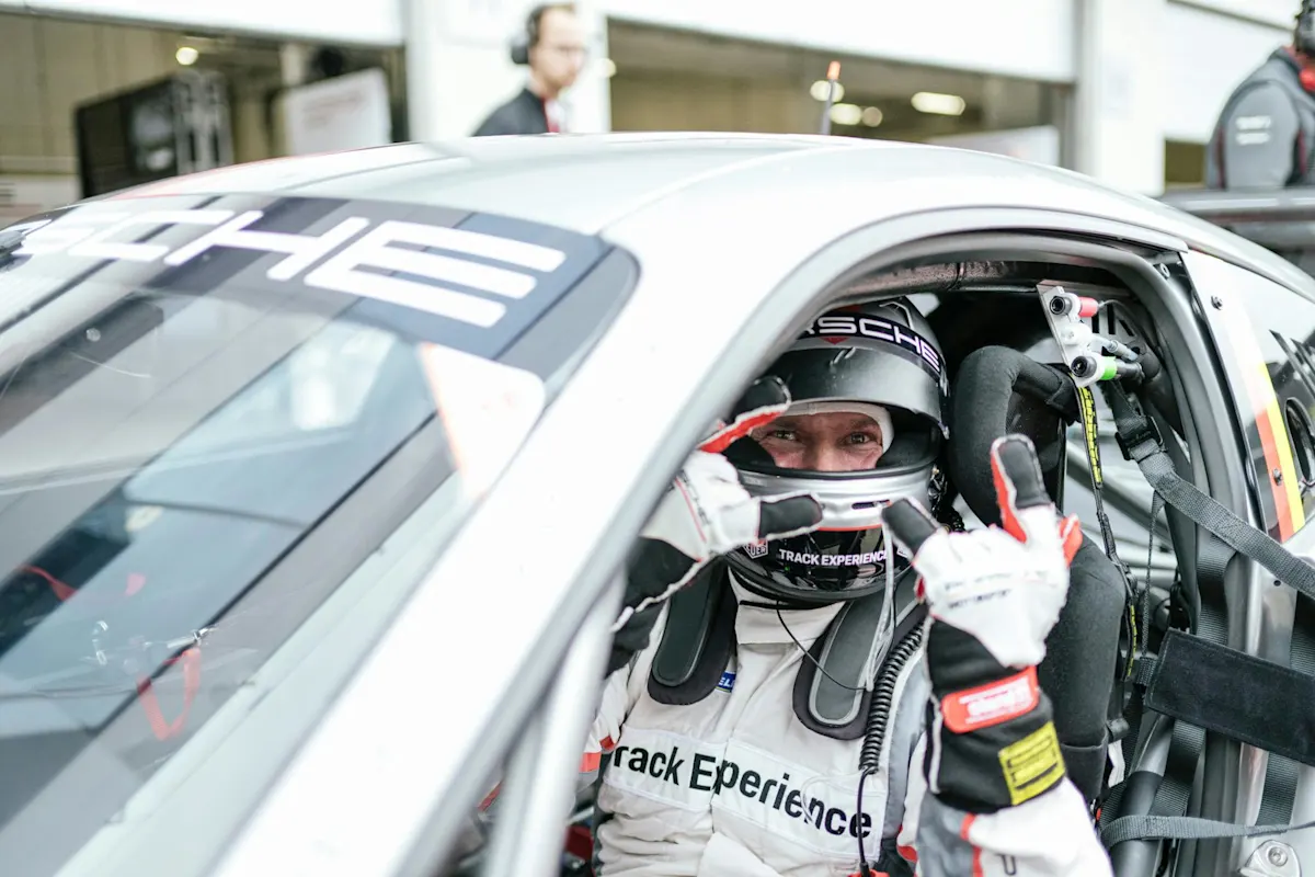 Rennfahrer im Porsche gibt Daumen hoch im Track Experience-Outfit.