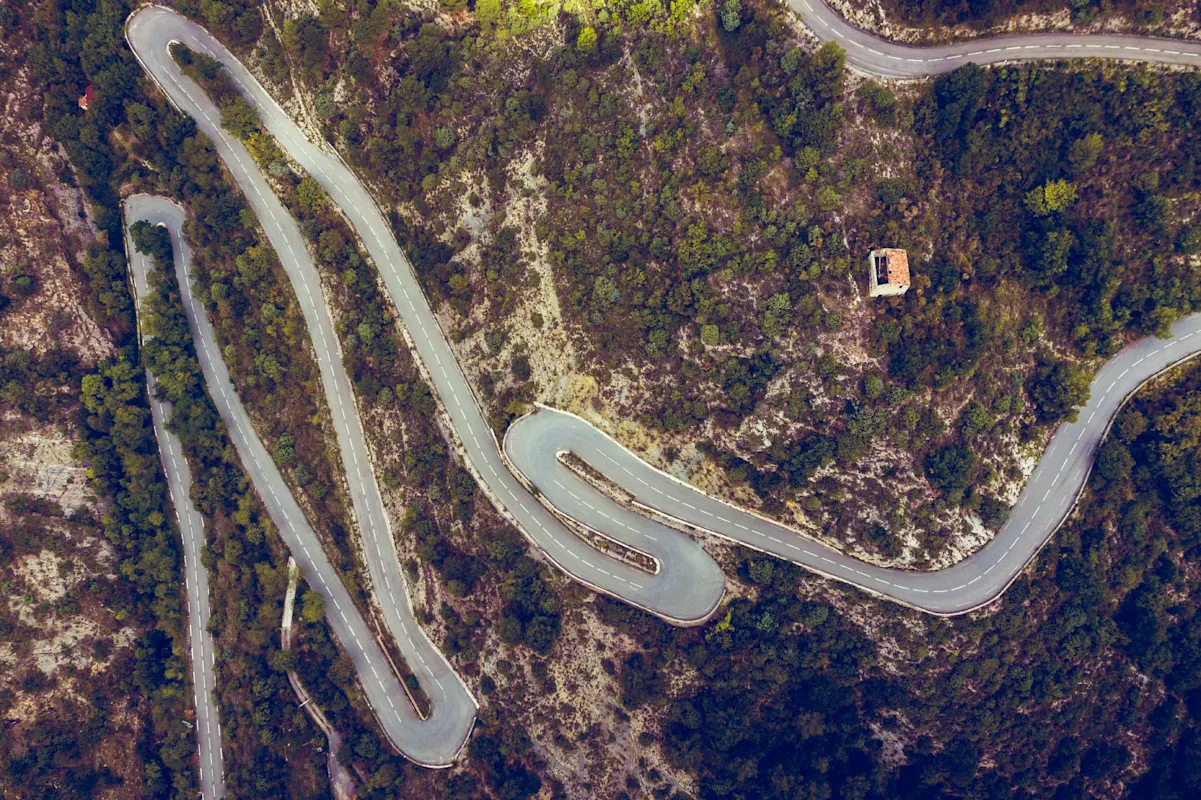 Luftaufnahme einer kurvigen Bergstraße durch üppiges Grün mit Gebäude auf Hügel.