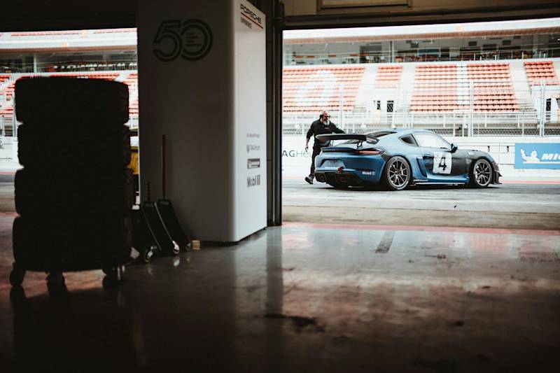 Person pushing a blue Porsche race car onto the track in a dimly lit garage.