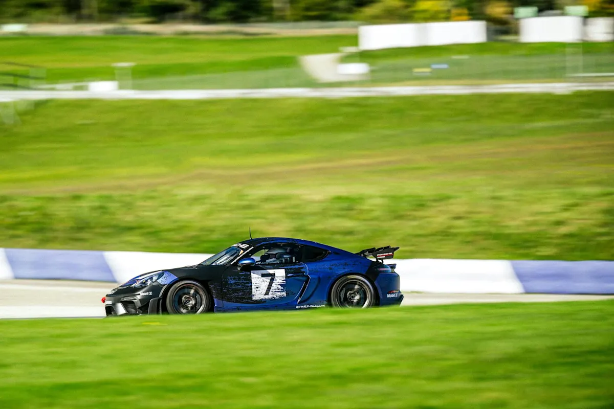 Blauer und schwarzer Porsche fährt auf Strecke mit grünem Hintergrund.