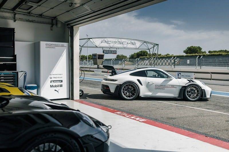 A white Porsche in a racetrack garage, with sunny sky and trees in the background.