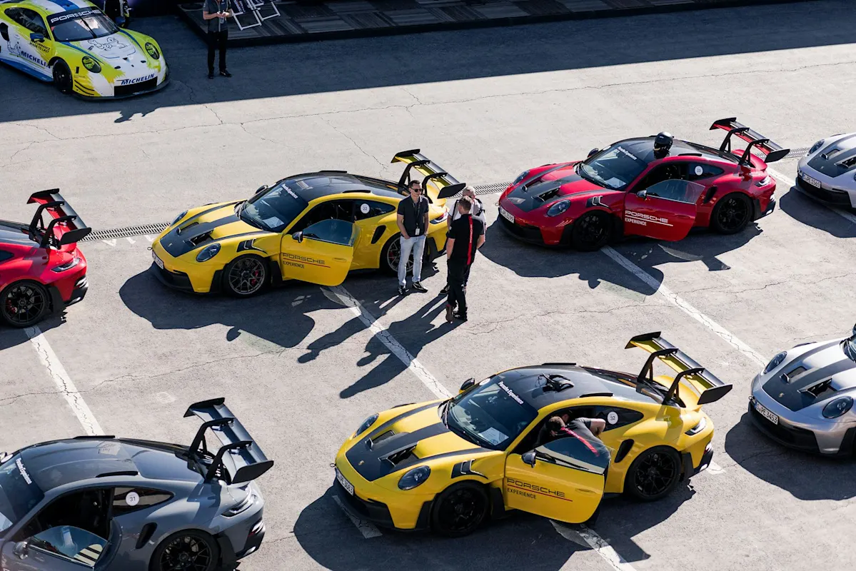 Aerial view of Porsche sports cars in yellow, red, and gray, with people nearby.
