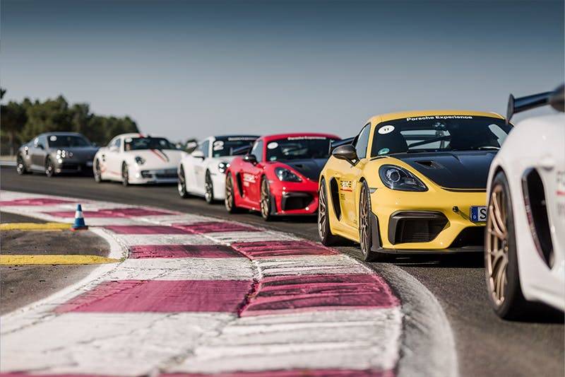 Porsche-Sportwagen rasen auf der Rennstrecke mit pinken und weißen Curbs unter klarem Himmel.