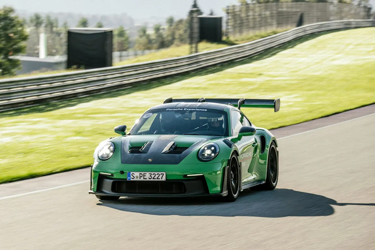 Porsche Sportwagen mit schwarzen Akzenten auf Rennstrecke umgeben von Grün und verschwommenem Hintergrund.