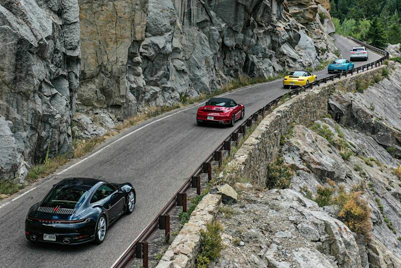 Porsche Sportwagen in verschiedenen Farben fährt auf einer malerischen Bergstraße mit Grünflächen, Klippen und Leitplanken.