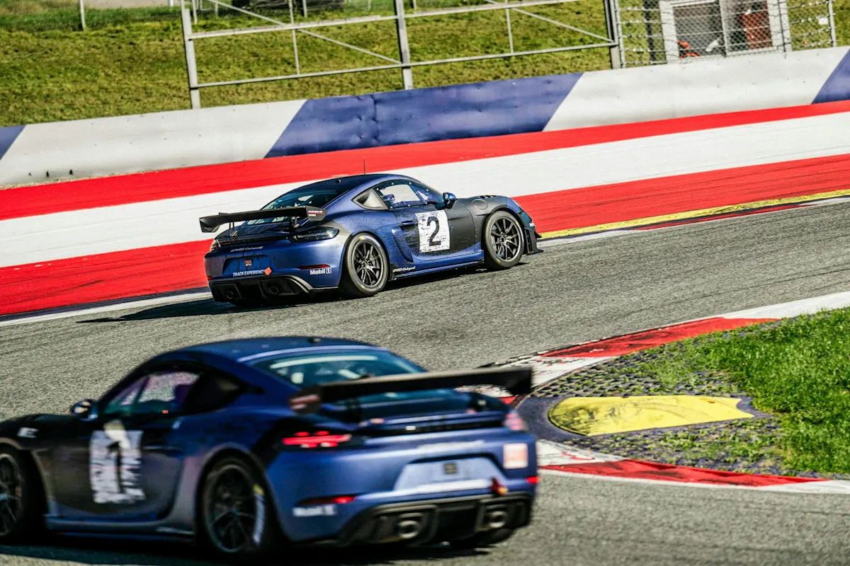 Porsche race car with number 2 leads on track with red and white barriers, under sunny skies with green grass.