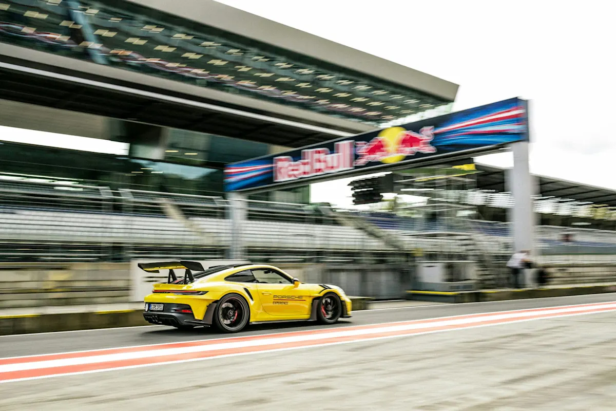 Gelber Porsche-Rennwagen rast an der Boxengasse vorbei auf der Rennstrecke mit verschwommener Bewegung und Tribüne.
